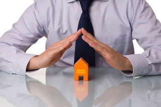 A man forming a triangle with his hands over a small building model.